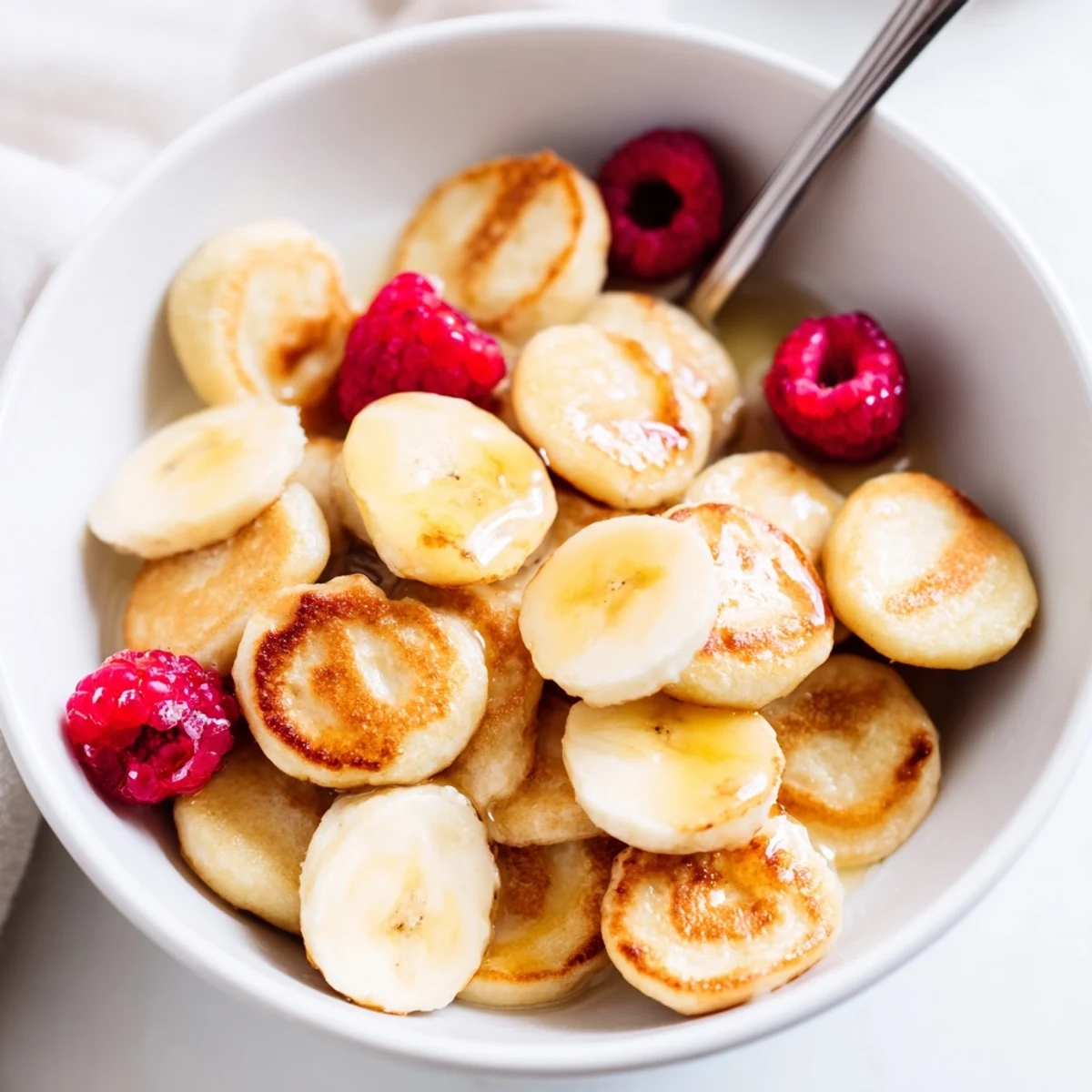 Mini pancake cereal topped with fresh berries and drizzled maple syrup.  