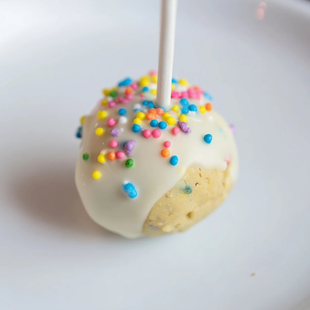 Close-up of a lightened-up sugar cookie cake pop, coated in white chocolate and covered in festive sprinkles.