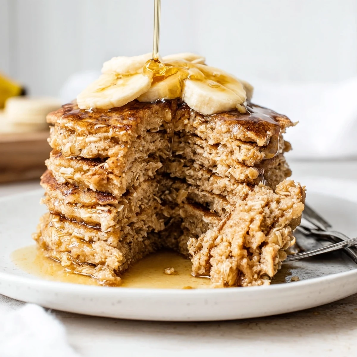 Fluffy banana oat pancakes topped with maple syrup and sliced bananas on a rustic wooden board.  