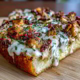 Slice of Marry Me Chicken pizza showing a rich Parmesan cream sauce and tender diced chicken on a rustic wooden board.