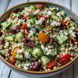 Fresh parsley and a zesty oregano vinaigrette finish this Mediterranean Pearl Couscous, served in a rustic white bowl for a light, healthy lunch.  