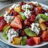 Vibrant rainbow fruit platter with strawberries, pineapple, kiwi, and blueberries served with fluffy coconut whipped cream.  