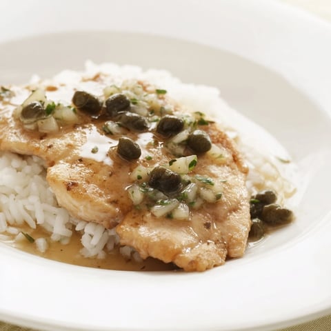 Golden-brown chicken piccata nestled in a bowl atop fluffy rice, ready to eat and enjoy.