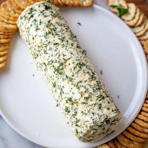 Herb-coated cheese log with vibrant green herbs, ready to be served with assorted crackers.