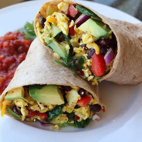 A colorful, veggie-loaded breakfast burrito: layers of eggs, vegetables, and avocado, ready to eat.