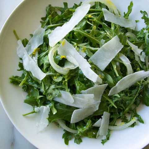 Fresh arugula salad with bright lemon dressing, Parmesan shavings perfectly displayed.