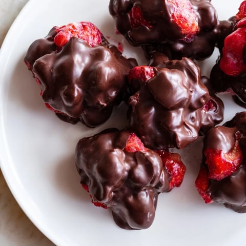 Frozen strawberry yogurt clusters, coated in dark chocolate, a refreshing dessert.