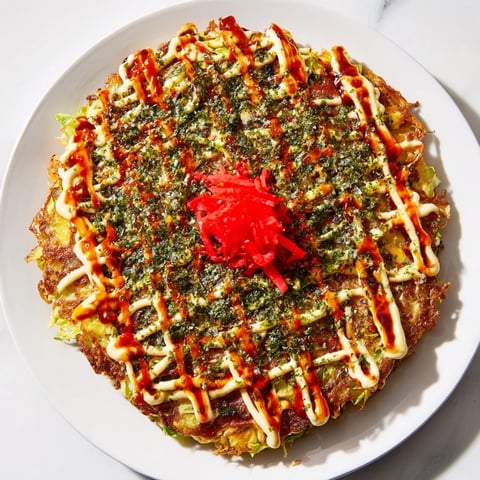 Golden Japanese Okonomiyaki Pancakes sizzle in a skillet, topped with creamy mayonnaise, tangy sauce, and dancing bonito flakes.