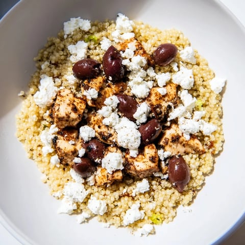 A Mediterranean Chicken Bowl in a ceramic bowl with grilled chicken, cherry tomatoes, feta, and olives on fluffy quinoa.