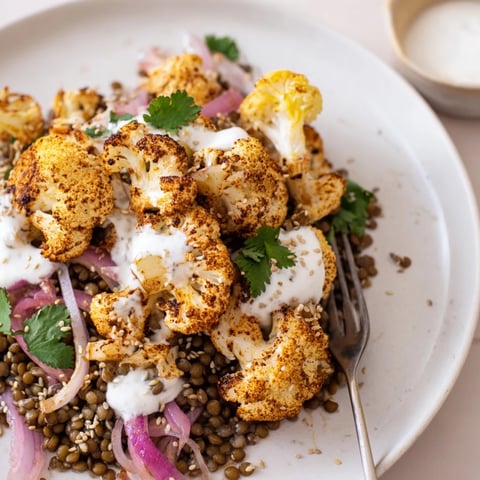 Golden roasted cauliflower florets arranged over a bed of lemony lentil salad, drizzled with creamy cumin-tahini yogurt and topped with fresh parsley.