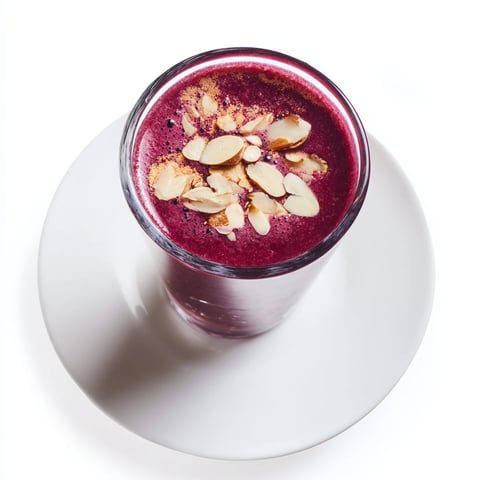 A tall glass of Cherry Almond Smoothie, creamy and pink with almond milk, topped with fresh cherries and slivered almonds.