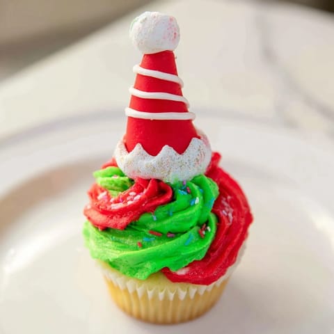 A towering display of Elf Hat Cupcakes, buttercream swirled with bright fondant hats, ready to enjoy.