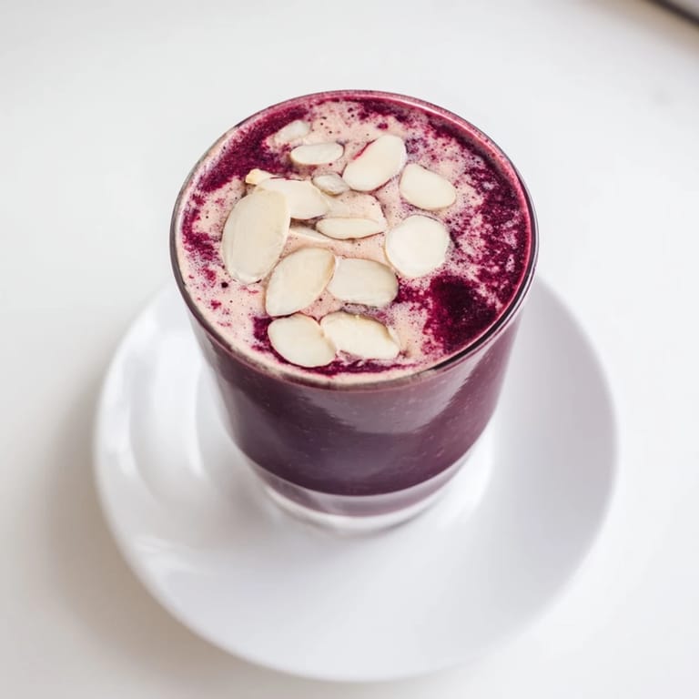 Close-up of Cherry Almond Smoothie in a glass, frosty and thick, garnished with a sliced banana and toasted almond slices.