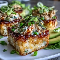 Crispy golden rice squares topped with creamy spicy tuna and fresh avocado slices for a vibrant sushi-inspired appetizer.